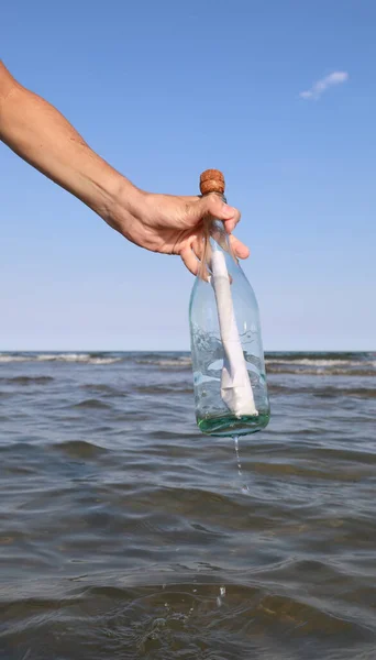 hand takes a bottle with secret message inside on the sea