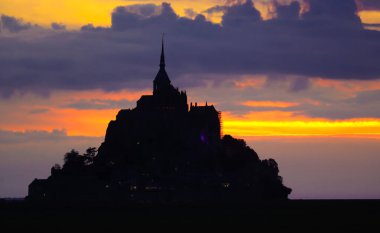 Silhouette of the famous Mont Saint Michel Abbey in Normandy in France and the colors of the clouds at sunset