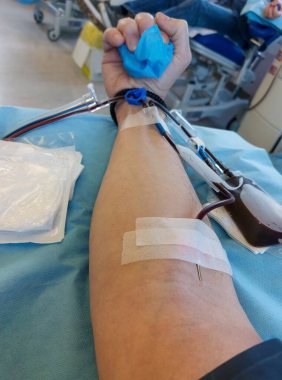 young blood donor with large needle stuck in forearm during donation at hospital