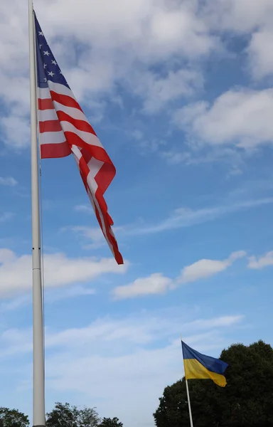 american flag and in the background the flag of ukraine waving in daytime and blue sky