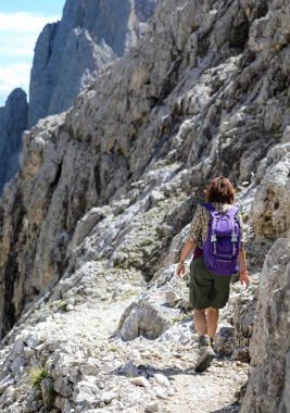 Young female hiker walks with backpack on stony path on European alps in Northern Italy