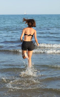 Young girl runs on the water of the sea raise many splashes in summer