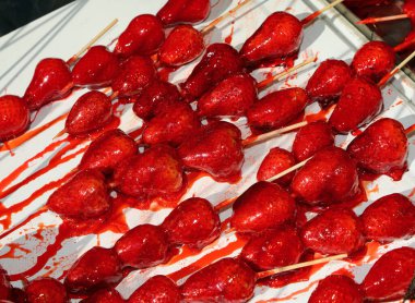skewers of large red ripe caramelized strawberries with sugar on top for sale in candy stall