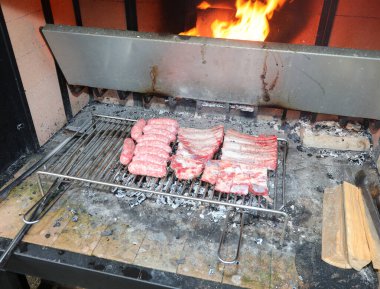 Barbekü, sosis ve domuz pirzolasından oluşan büyük metal ızgara ateşle pişiriliyor.