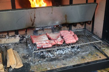 Barbekü, sosis ve domuz pirzolasından oluşan büyük metal ızgara odun ateşiyle pişiriliyor.