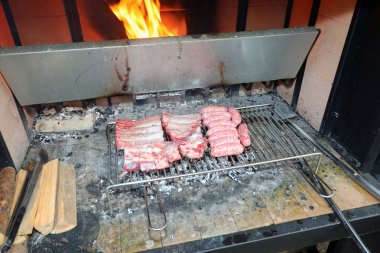 Barbekü, sosis ve domuz pirzolasından oluşan büyük metal ızgara odun ateşiyle pişiriliyor.