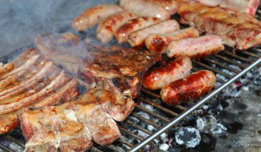 Açık hava barbeküsünün büyük metal ızgarası, sosisler ve közün üzerinde pişmiş domuz pirzolası.