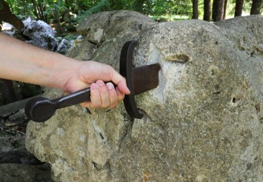 Şövalyenin eli ormanın ortasındaki kayadan sihirli kılıcı çıkarmaya çalışıyor.