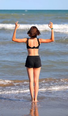 Genç kız yaz aylarında deniz kıyısında OM sembolüyle jimnastik ve yoga meditasyonu yapıyor.