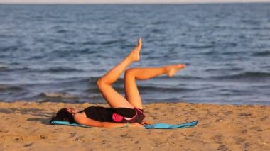 Spor kıyafetli genç kız sahilde jimnastik yapıyor.