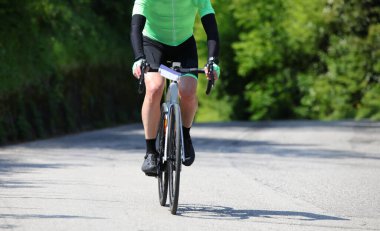 Kırsalda asfalt yolda bisiklet süren yalnız bisikletçi pedalları gün boyunca antrenman yapıyor.