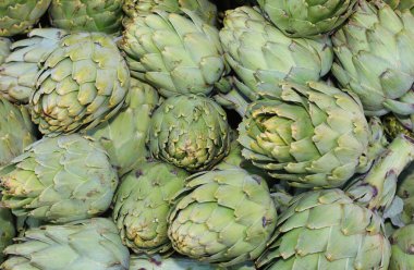 background of many  green large ripe artichokes for sale at market