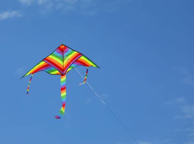 colorful kite of many colors of the rainbow flies tied to a thread in the blue sky symbol of childhood and carefreeness clipart