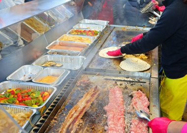 Sokak yemekleri tezgahı sosisli piadinalar, pişmiş etler ve ızgara sebzeler hazırlıyor.
