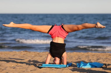athletic slender girl by the sea does gymnastic training with head down to strengthen muscles
