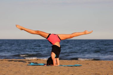 athletic slender girl by the sea does gymnastic training with head down to strengthen muscles