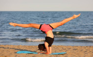 athletic slender girl by the sea does gymnastic training with head down to strengthen muscles