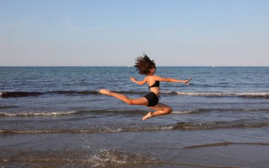 Genç atletik kız yazın deniz kıyısında çok uzun bir sıçrama yapar.