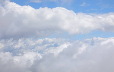 Bir sürü beyaz bulut ve mavi gökyüzü yüksek uçan bir uçağın üstünden görünüyor.