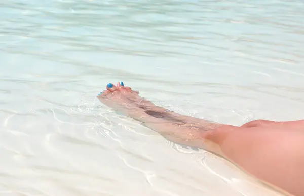 long slender legs of the woman relaxing in the water and toenails with blue polish