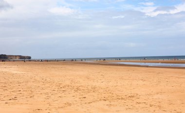 Geniş kumlu bir sahil manzarası ve yazın arka planda deniz çok küçük insanlarla birlikte.