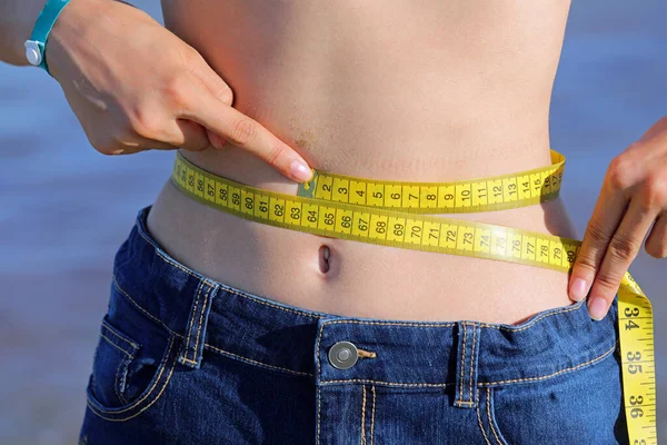 一个年轻女孩的腹部测量她的腰围 黄色的带子测量数厘米 — 图库照片