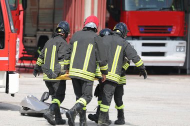 İtfaiyeciler kazadan sonra yaralı kişiyi sedyeyle taşıyorlar ve kırmızı itfaiye aracı.