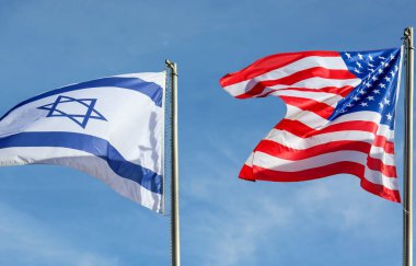 Mavi gökyüzünde rüzgarda sallanan Amerikan ve İsrail bayrakları