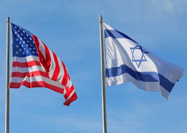 Mavi gökyüzünde rüzgarda sallanan Amerikan ve İsrail bayrakları