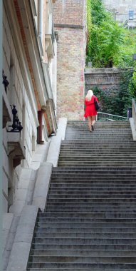 Kırmızı etekli genç bir kadın binaların ortasındaki merdivenlerden çıkıyor.