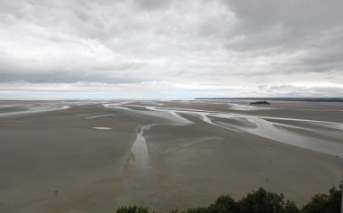 Kuzey Fransa, Normandiya 'daki Mont Saint Michel Manastırı' ndan yükselen panoramik manzara ve alçak gelgitte kumsalda yürüyen küçük insanlar