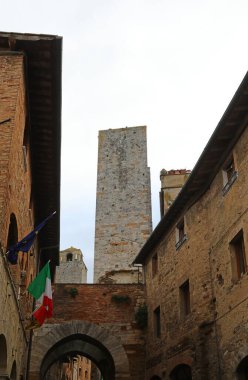 İtalya 'da Siena yakınlarındaki San Gimignano şehrinin duvarcılığından yapılmış antik kuleler ve İtalyan bayrağı.