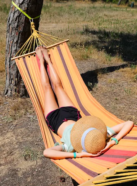 Young girl on the hammock in the summer with a big straw hat and bare feet while resting