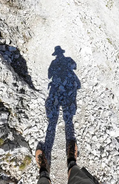 shadow of hiker with hat and his boots to walk in the stony path in high mountains