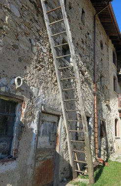 Kırsal bir ortamda eski ahırın duvarına eğimli bir şekilde yerleştirilmiş uzun tahta merdiven.