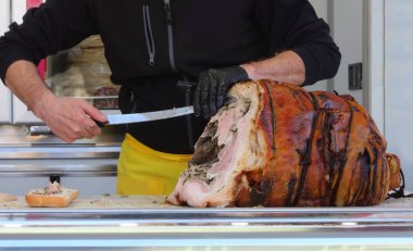 Bir şarküteri işçisinin eldivenli eli büyük bir bıçakla kavrulmuş porchetta dilimliyor.