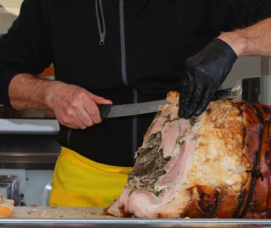 Bir şarküterinin eli şarküteride büyük bir bıçakla kavrulmuş porchetta dilimliyor.