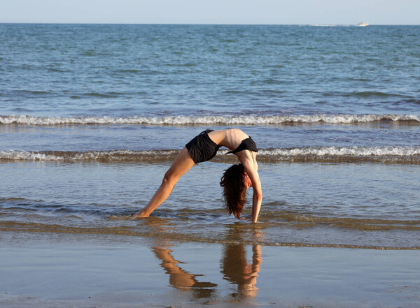 young girl performs gymnastic exercises arching her back and forming a heart in the reflection on water