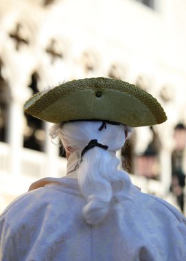 Çok kalın peruklu maskeli biri ve Venedik Karnavalı sırasında arka planda antik bir saray.
