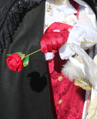 Kırmızı eldivenli bir aşık eli, zamanı kolluyor çünkü sevgilisi geç kaldı ve kırmızı bir gül veriyor.