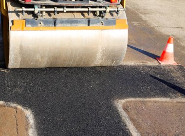 Bir trafik konisi ve asfalt silindirli inşaat alanı