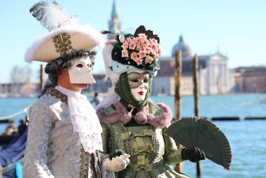Venice, VE, Italy - February 13, 2024: couple with Venetian Mask at the Venice Carnival and adriatic sea on background clipart