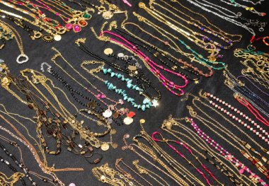 many necklaces and bracelets and anklets for women of golden metallic material with precious stones or pearls and pendants for sale in the shop in the shopping center clipart