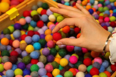 Hobi dükkanında kişiselleştirilmiş bir kolye yaratmak için elinde haşlanmış yünden yapılmış kırmızı bir top tutan genç bir kızın eli.