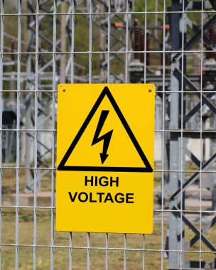 yellow sign with the big text high voltage with the triangle and the lightning outside the electrical substation clipart