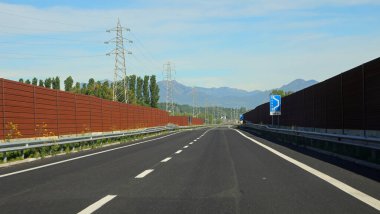 wide asphalted highway with very little traffic and noise barriers clipart