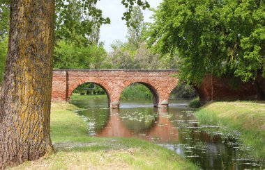Ancient bridge made of red bricks with three arches over the river on the forest clipart