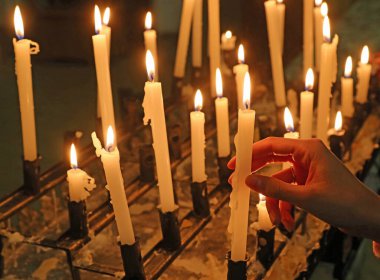 female hand holding a lit candle in a church amidst a sea of flickering flames from the candles of devout pilgrims clipart