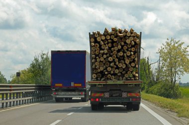 Log truck on the highway being overtaken by a blue truck clipart