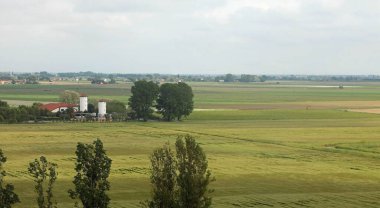 Panoramic view of the plain with vast cultivated fields and no hills on the horizon and a farm clipart